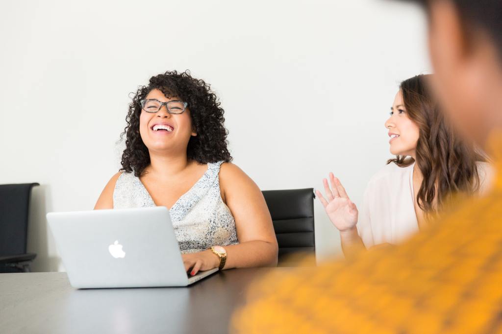 young woman in a conference room at a laptop laughing with some co-workers
